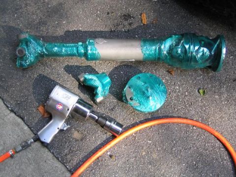 1979 Ford Bronco - A driveshaft, its U-joints, and a flange are wrapped in green tape, alongside an air-powered impact wrench and orange hose.