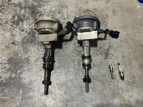 1996 Ford Bronco - Two automotive distributors and two spark plugs are laid out on a concrete surface.