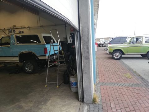 1996 Ford Bronco - Two Ford Broncos are visible, one in a garage and another parked outside on a brick-paved area.
