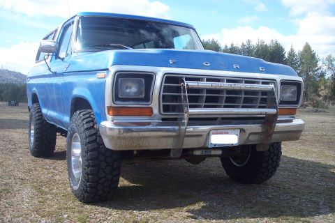1978 Ford Bronco - A blue 1978 Ford Bronco sits on a dirt lot, equipped with large off-road tires and a front grille guard.