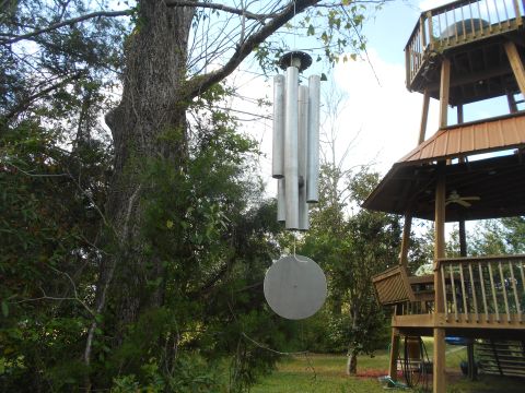 1992 Ford Bronco - Wind chimes are suspended from a tree branch, with a wooden deck structure visible to the right.