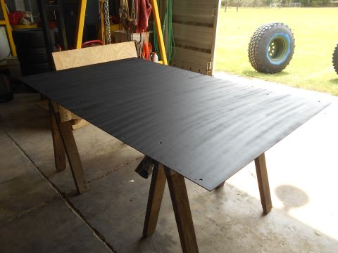 1992 Ford Bronco - A large black sheet of metal rests on sawhorses in a garage, with a large off-road tire visible in the background.