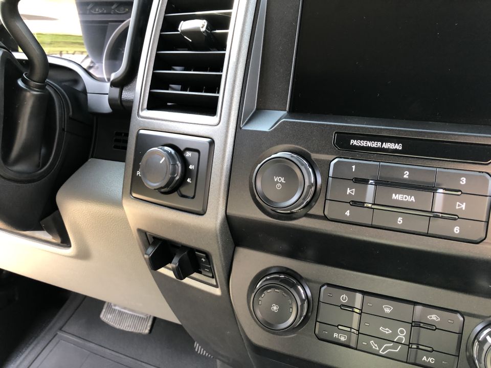 Close-up of a truck's dashboard with a 4x4 selector, volume knob, media buttons, and climate controls