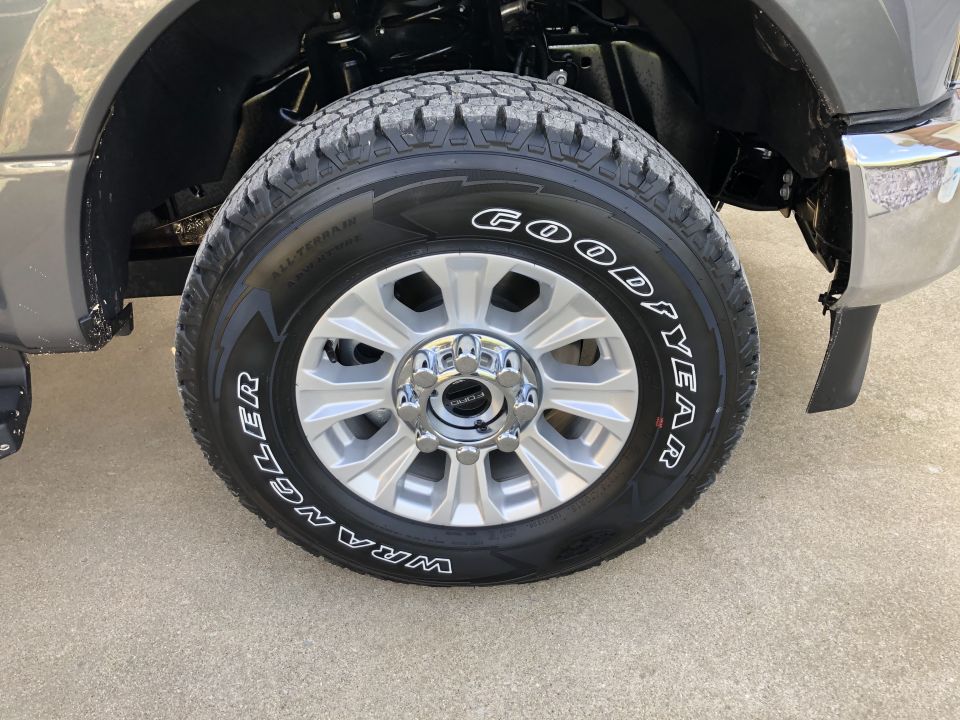 Gray Ford F-250 front wheel with Goodyear Wrangler All-Terrain tires and chrome lug nuts. The vehicle is gray