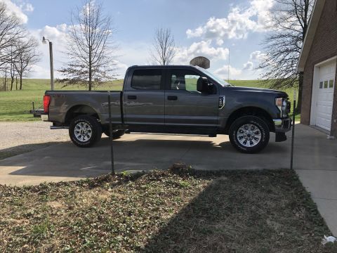 2021 Ford F-250 - This gray Ford F-250 Super Duty pickup truck is parked on a concrete driveway beside a brick house with a garage door.