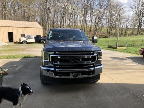 2021 Ford F-250 - A dark Ford Super Duty truck is parked in a driveway with a dog nearby and another vehicle in the background.