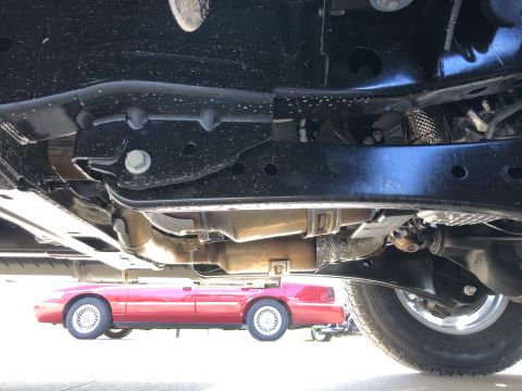 2021 Ford F-250 - The underside of a truck reveals a red sedan parked beneath it, with visible exhaust and drivetrain parts.