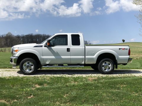 2011 Ford F-250 - A white Ford Super Duty pickup truck is parked on a gravel driveway with grassy fields and trees in the background.