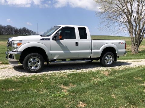 2011 Ford F-250 - A white 2011 Ford F-250 Super Duty pickup truck is parked on a gravel surface next to a grassy field.