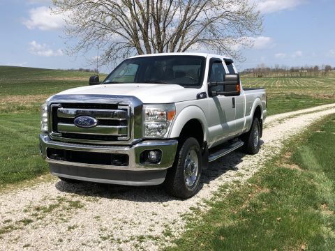 2011 Ford F-250 - White 2011 Ford F-250 Super Duty pickup truck parked on a gravel driveway with a field in the background.