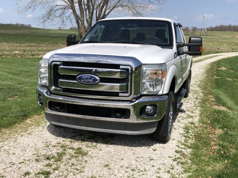 2011 Ford F-250 - A white Ford Super Duty truck is parked on a gravel road with a grassy field and trees in the background.