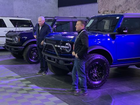 2021 Ford Bronco - Two men stand next to a blue 2021 Ford Bronco at an indoor event, with other Broncos visible in the background.
