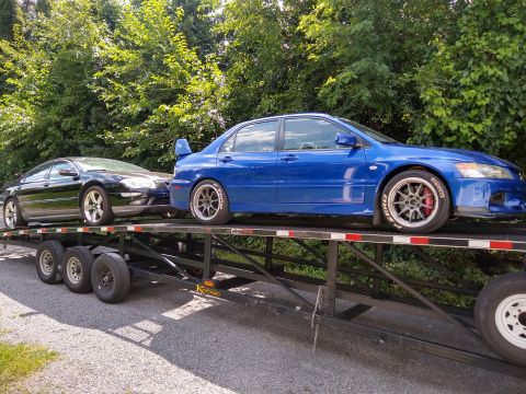 2006 Mitsubishi Evolution - A blue Mitsubishi Lancer Evolution and a black sedan are transported on a car hauler trailer.
