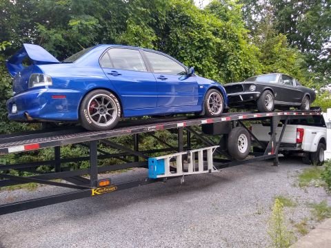 2006 Mitsubishi Evolution - Two cars, a blue Mitsubishi Evolution and a black Ford Mustang, are transported on a car hauler.