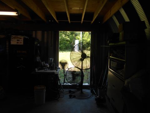 1992 Ford Bronco - Three large fans are positioned in a dimly lit garage, with an open doorway revealing a sunlit outdoor scene.