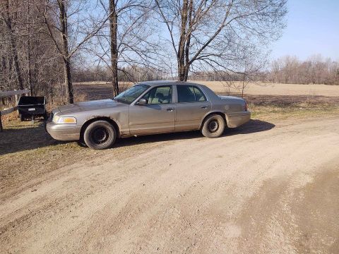 2005 Ford Crown Victoria - Side view of a 2005 Ford Crown Victoria with steel wheels and visible rust on the body.