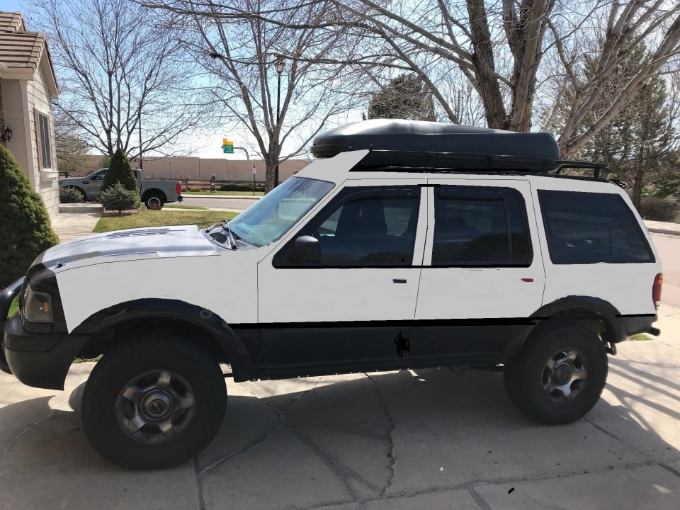 Side view of a white SUV with a black roof box and black trim. It has off-road tires and fender flares