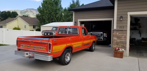 1977 Ford F-150 - An orange 1977 Ford F-150 pickup truck is parked in front of a garage, with another truck visible inside.
