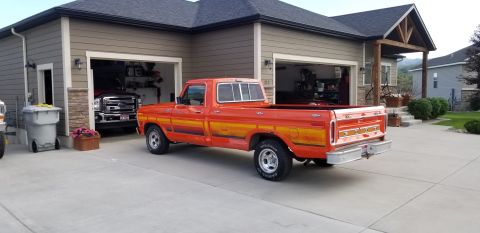 1977 Ford F-150 - This orange 1977 Ford F-150 pickup truck features distinctive side stripe graphics and is parked in a driveway next to a garage.