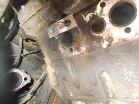 1992 Ford Bronco - Close-up view of an engine block showing exhaust manifold bolt holes and a metal mounting plate with a bolt.