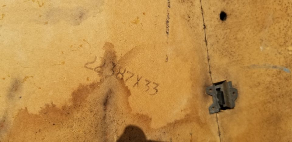 Stenciled numbers 22387X33 on a tan, textured surface with a metal bracket attached