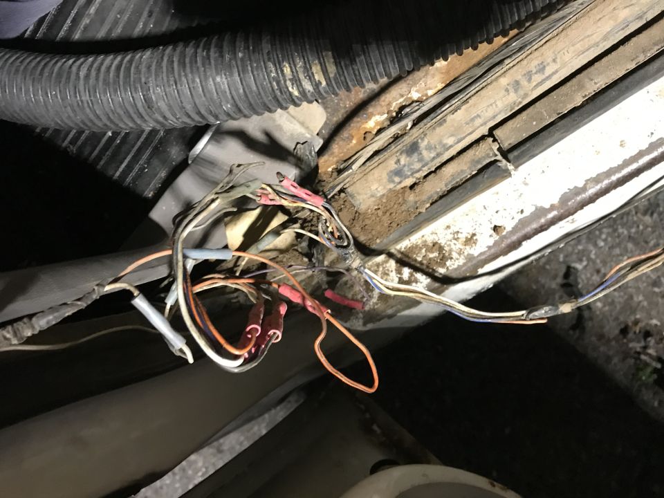 Damaged frayed automotive wiring harness with exposed colored wires by rusty rail