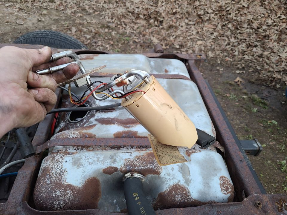 Hand holding a removed fuel pump assembly over a rusty fuel tank