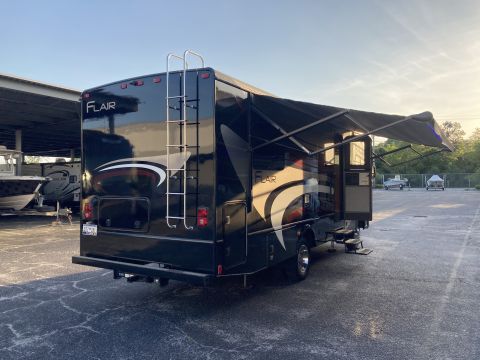 2015 Ford F-550 - Rear view of a black RV, identified as a Flair model, with its awning deployed and a ladder attached to the rear.