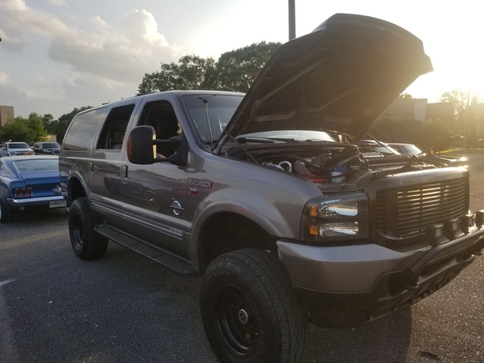 Gray Ford Excursion SUV, hood open, parked next to a blue classic car