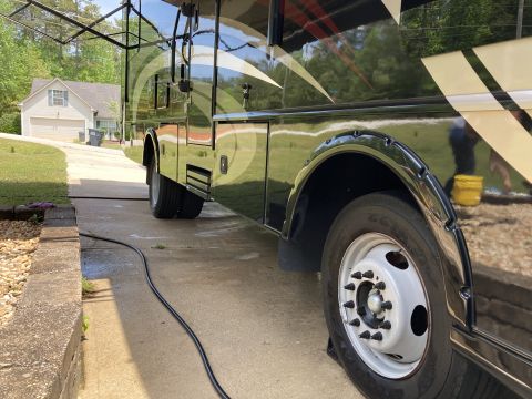 2015 Ford F-550 - A motorhome is parked on a concrete driveway, showing its side profile with dual rear wheels and distinctive graphics.