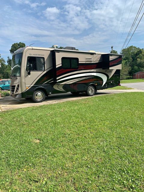 2015 Ford F-550 - A Fleetwood Flair motorhome is parked on a residential street. The vehicle has a beige and dark green exterior with red and white accents.