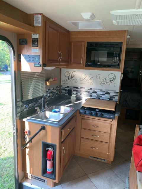 2015 Ford F-550 - RV interior features a compact kitchen with a sink, stovetop, and microwave, plus a fire extinguisher.