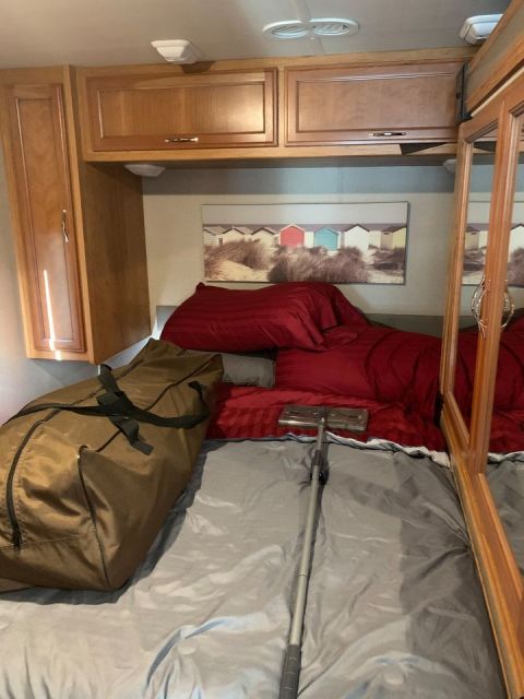 2015 Ford F-550 - Interior view of an RV, showing a bed with red linens and a vacuum cleaner on top.
