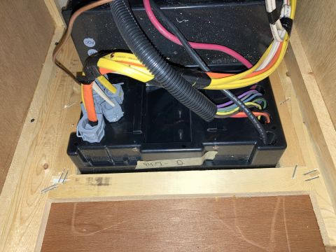 2015 Ford F-550 - Close-up of RV electrical converter and its wiring harness within a wooden enclosure.