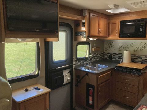2015 Ford F-550 - Interior view of an RV kitchen, showing a sink, stovetop, microwave, and television mounted above a window.