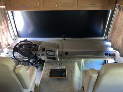 2015 Ford F-550 - RV cockpit showing a Ford steering wheel, tan dashboard, leather seats and overhead cabinets.