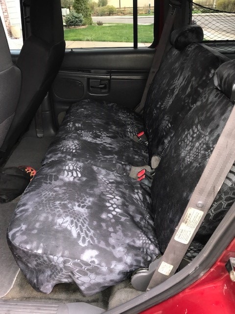 2000 Ford Explorer - Rear bench seat of an SUV fitted with a black-and-gray snake-pattern camo seat cover, doors open to a residential yard.