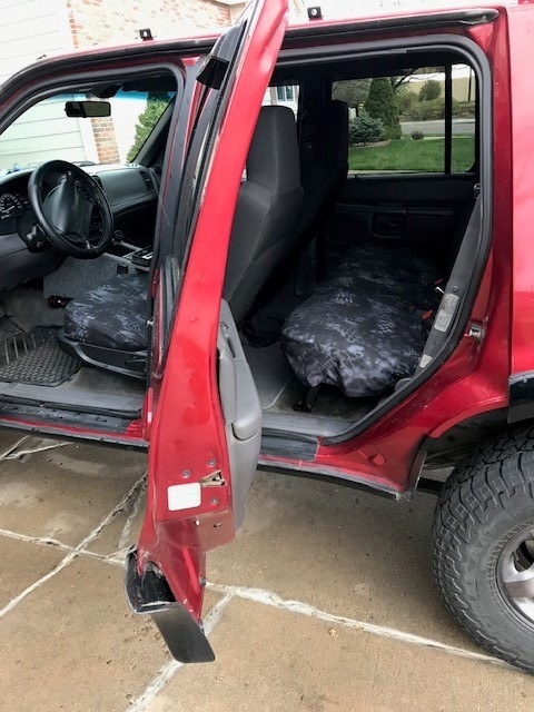 2000 Ford Explorer - Interior view of a red 2000 Ford Explorer, driver's side door ajar, revealing camouflage seat covers.