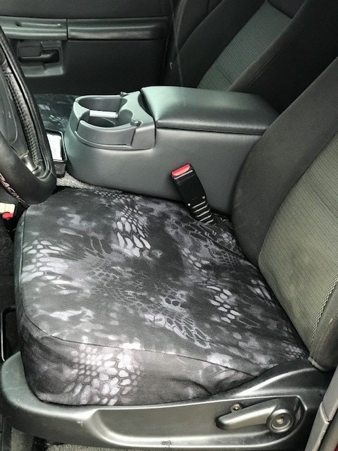 2000 Ford Explorer - Aftermarket Kryptek-pattern camouflage seat cover installed over the driver's seat, with center console cup holders and seatbelt buckle vis…