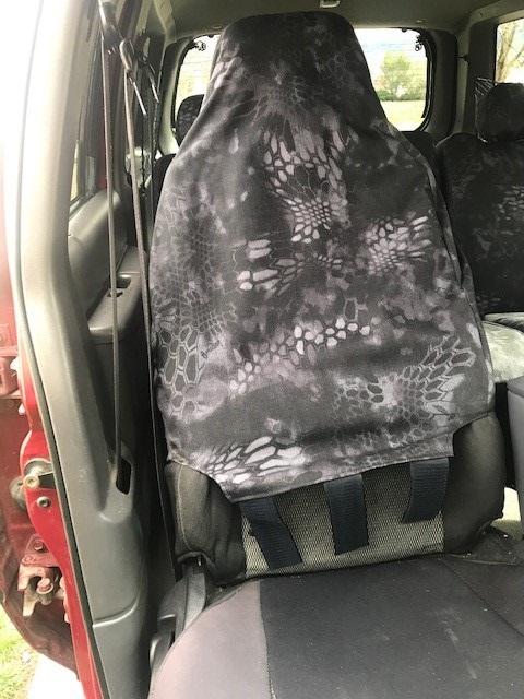 2000 Ford Explorer - Kryptek-style camouflage seat cover hung over a front seat inside a truck cab, with rear bench seat and red exterior body visible through t…