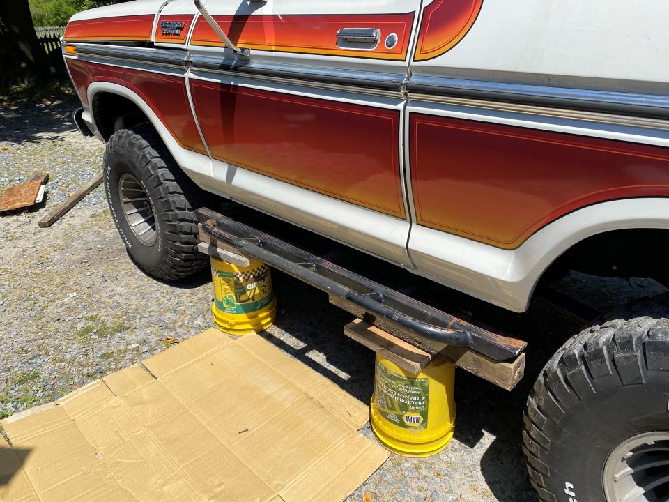 Side view of a 1979 Ford Bronco with orange and red stripe detail, lifted on yellow buckets