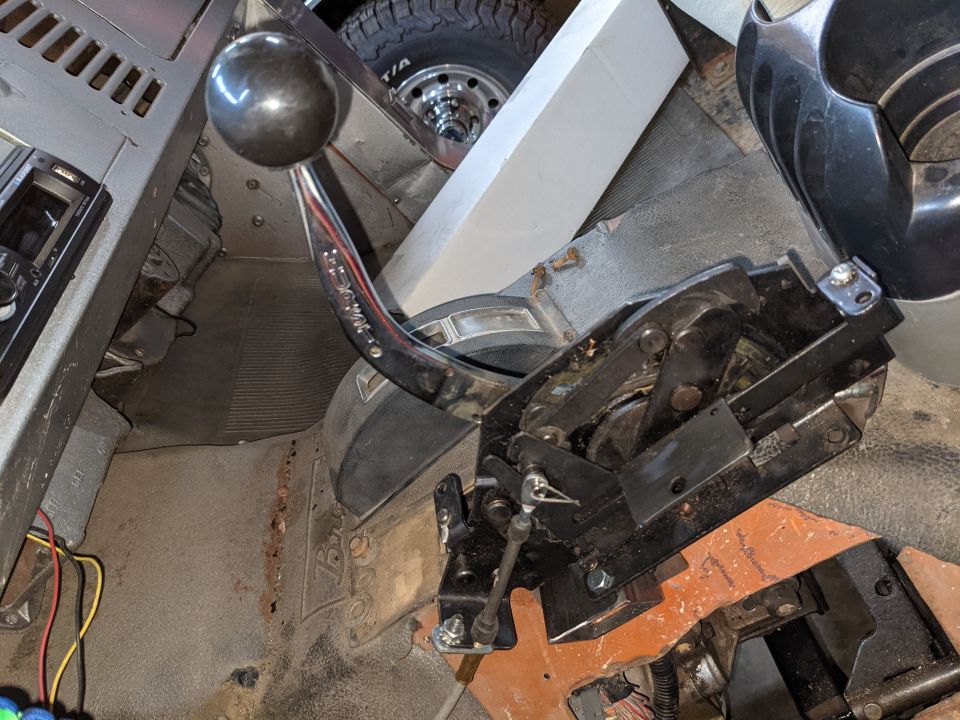 Manual shifter with black knob and chrome lever over a transmission tunnel with shifter linkage and floor mat