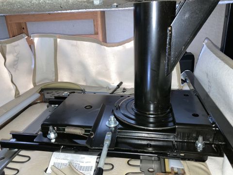 2015 Ford F-550 - The underside of a seat mechanism is shown, featuring a black metal swivel base with a central cylindrical post. A coiled spring and variou…