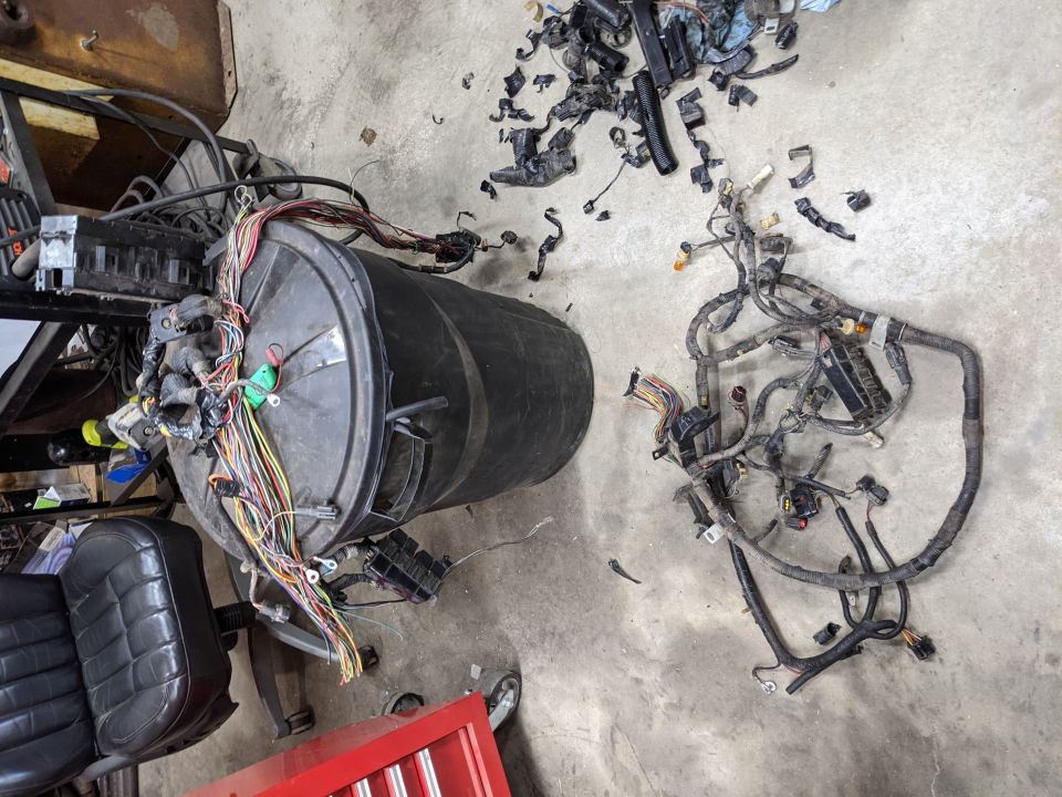 Vehicle wiring harnesses and connectors spread on garage floor next to trash can covered in stripped wires
