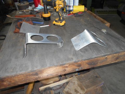 1992 Ford Bronco - Two custom aluminum brackets are displayed on a workbench alongside various tools and hardware.