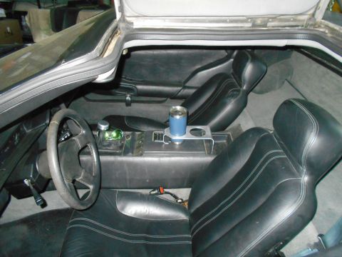 1992 Ford Bronco - The interior of a DeLorean DMC-12 is shown, featuring black leather seats with white stitching, a central console with a cup holder and a b…