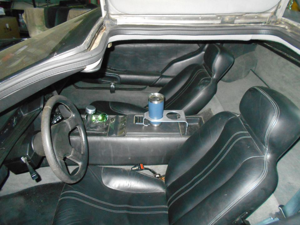 Interior view of a DeLorean DMC-12 with black leather seats and a blue tumbler in the cup holder.