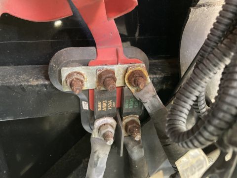 2015 Ford F-550 - Close-up view of two Buss AMG fuses, one 150A and one 125A, connected to a red battery terminal with rusted hardware. A black corrugated co…