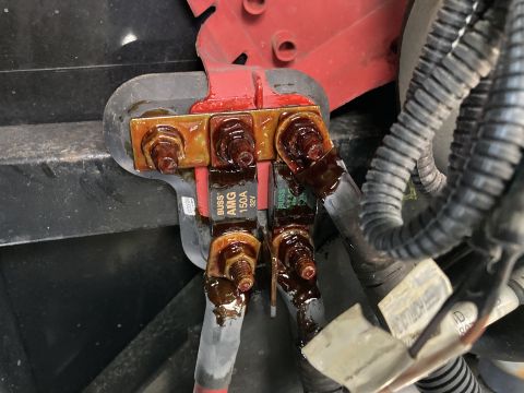 2015 Ford F-550 - A close-up view shows a red battery terminal bus bar with four large bolts and two Buss AMG 150A 32V fuses. Brown, greasy residue covers th…