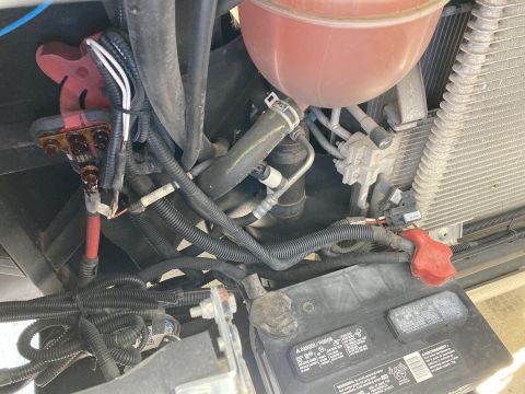 2015 Ford F-550 - A close-up view of a vehicle's battery and engine bay wiring, showing a red battery terminal cover and numerous black wire looms connected…